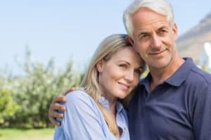 The image shows a middle-aged couple outdoors, embracing each other