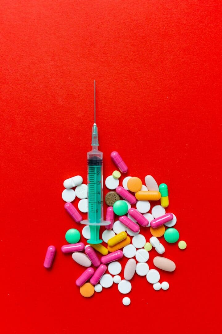 The image shows an injection surrounded by pills on a red background.