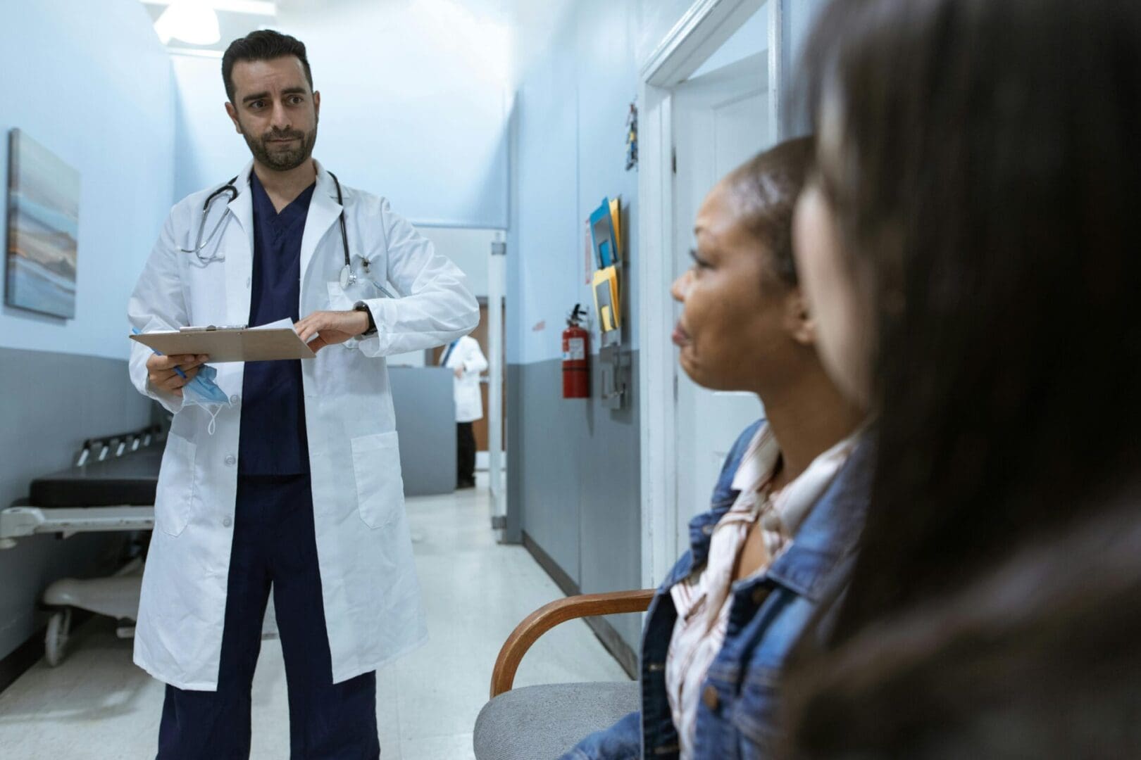 A Healthcare professional in a white coat discussing medical charts with a patient in a hospital hallway.