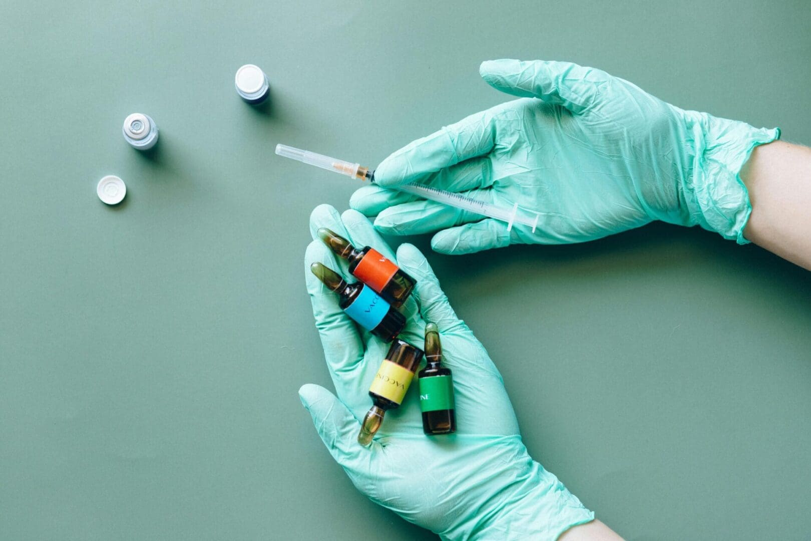 A Medical professional in blue globes holding a syringe and multiple colored medicine vials.