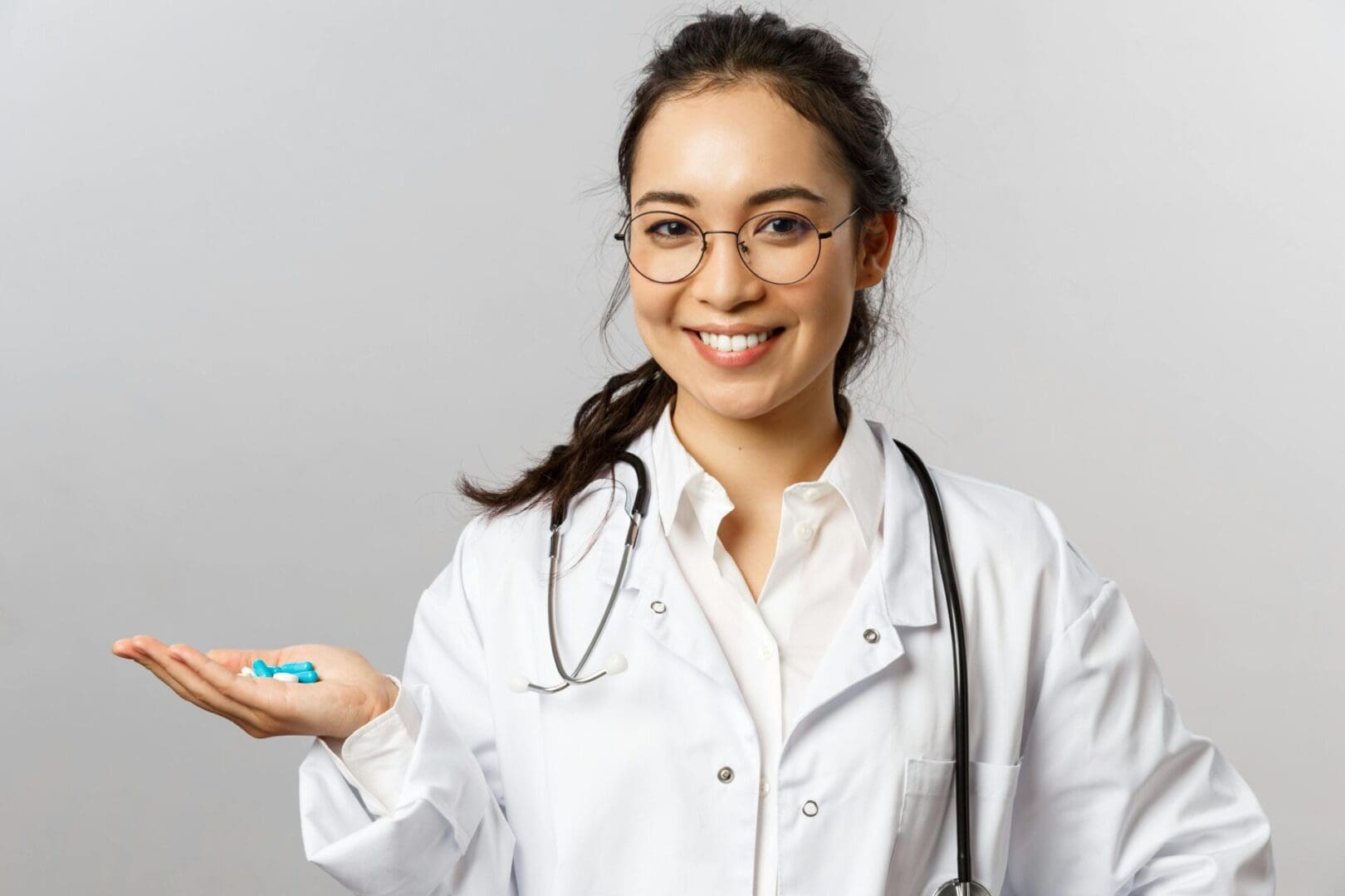 A Healthcare professional in a white coat holding blue pills in her right hand.