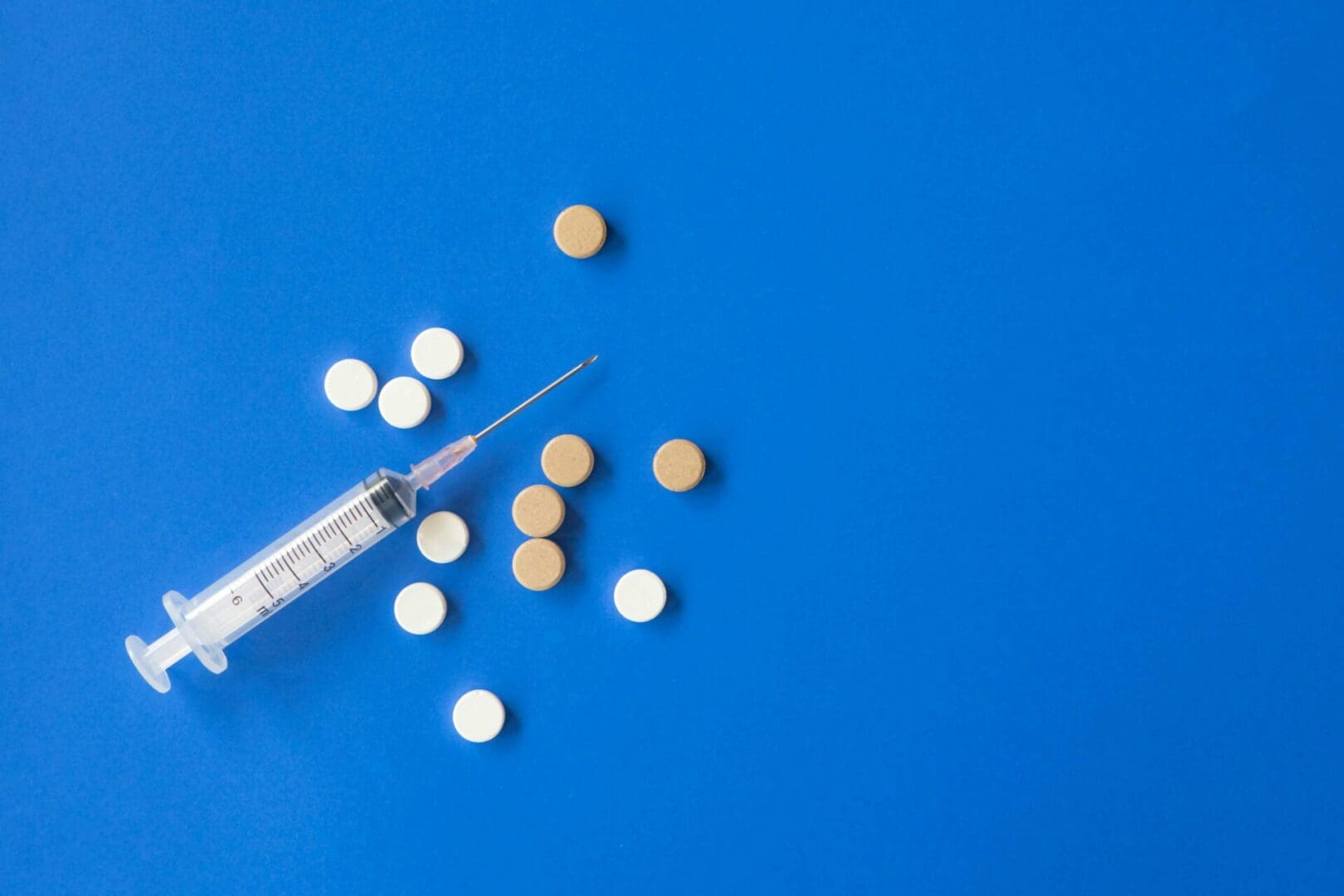 The image displays a syringe and several tablets placed on a blue sheet.