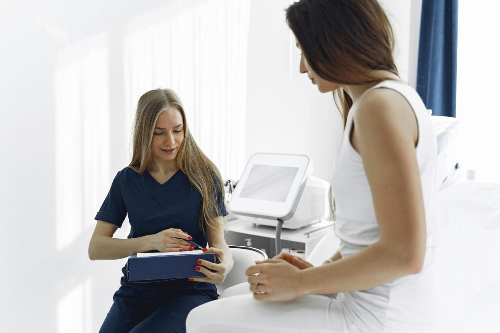 Medical specialist in blue scrubs discussing a treatment plan with a patient in a clinical setting.