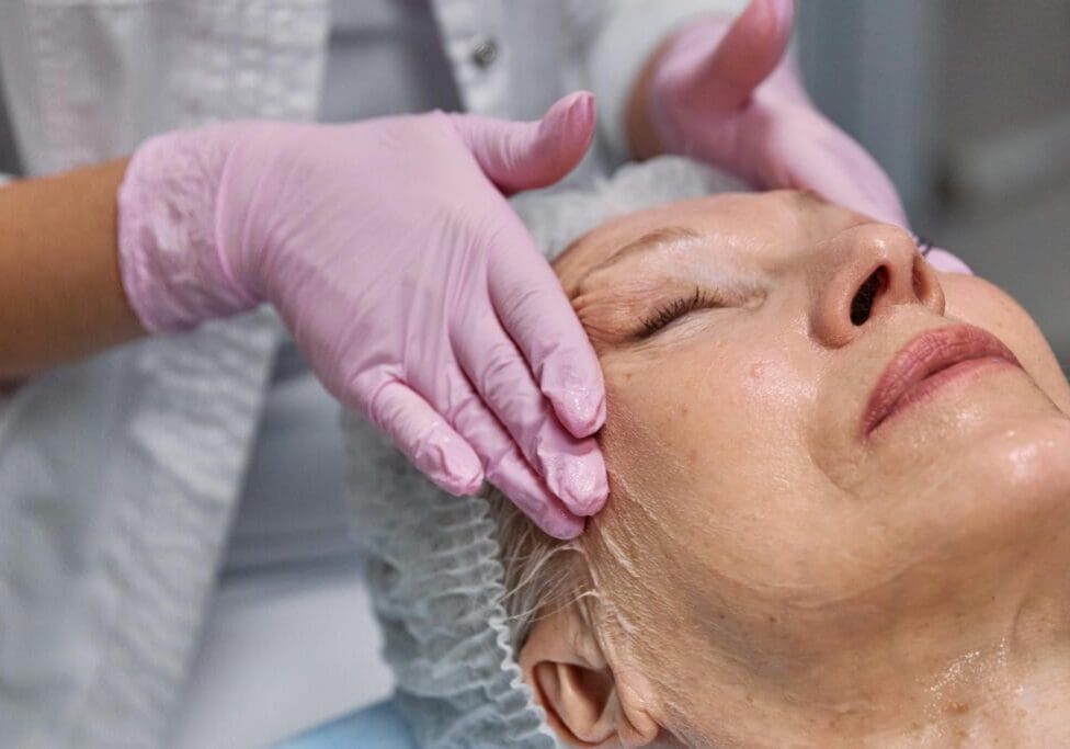 A healthcare provider performing a facial treatment on a woman in a clinical setting.