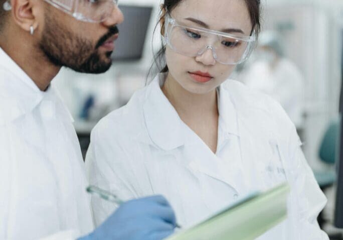 The image shows a couple of medical professionals in a white coat reviewing medical history in a laboratory setting.
