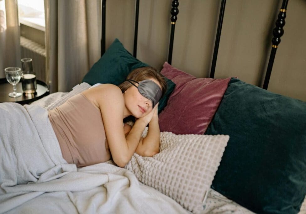 A Person resting in bed with a sleep mask and cozy pillows.