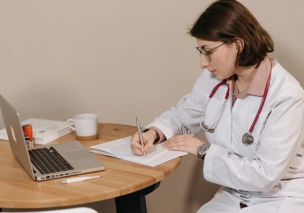 The image shows a Healthcare professional writing medical notes on paper.