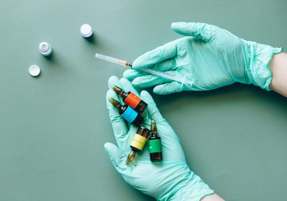 A Medical professional in blue globes holding a syringe and multiple colored medicine vials.