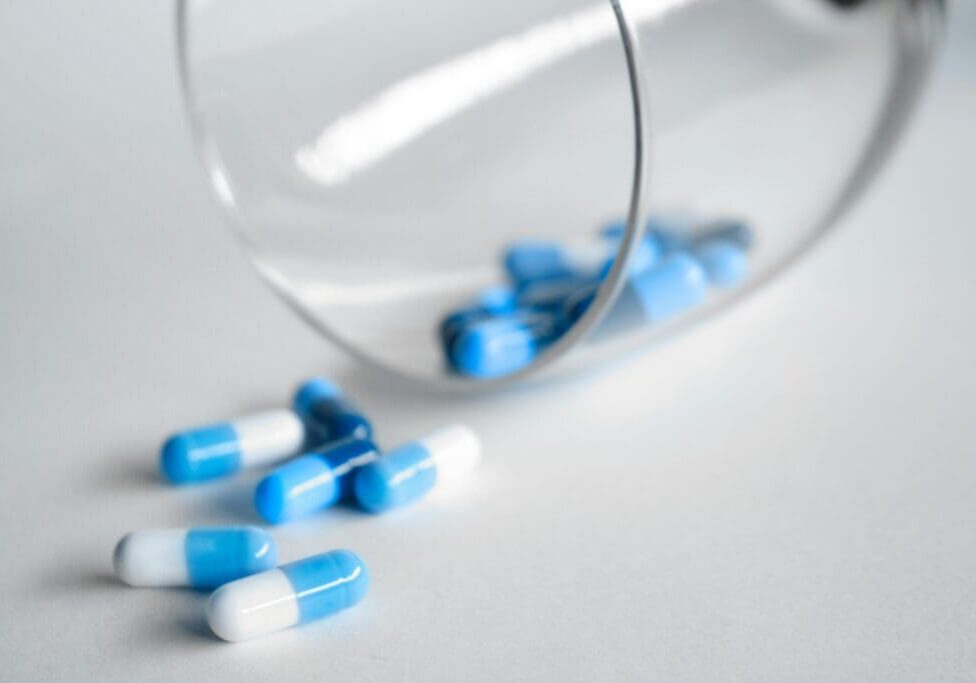 Blue and white capsules spilling from glass