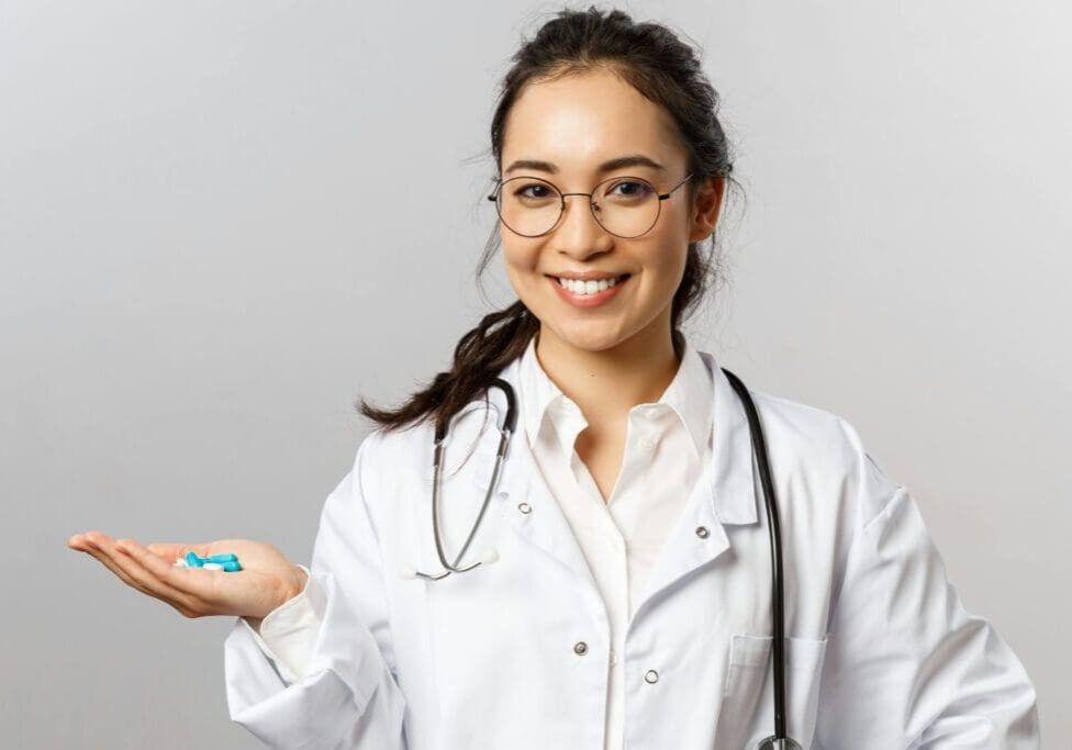A Healthcare professional in a white coat holding blue pills in her right hand.