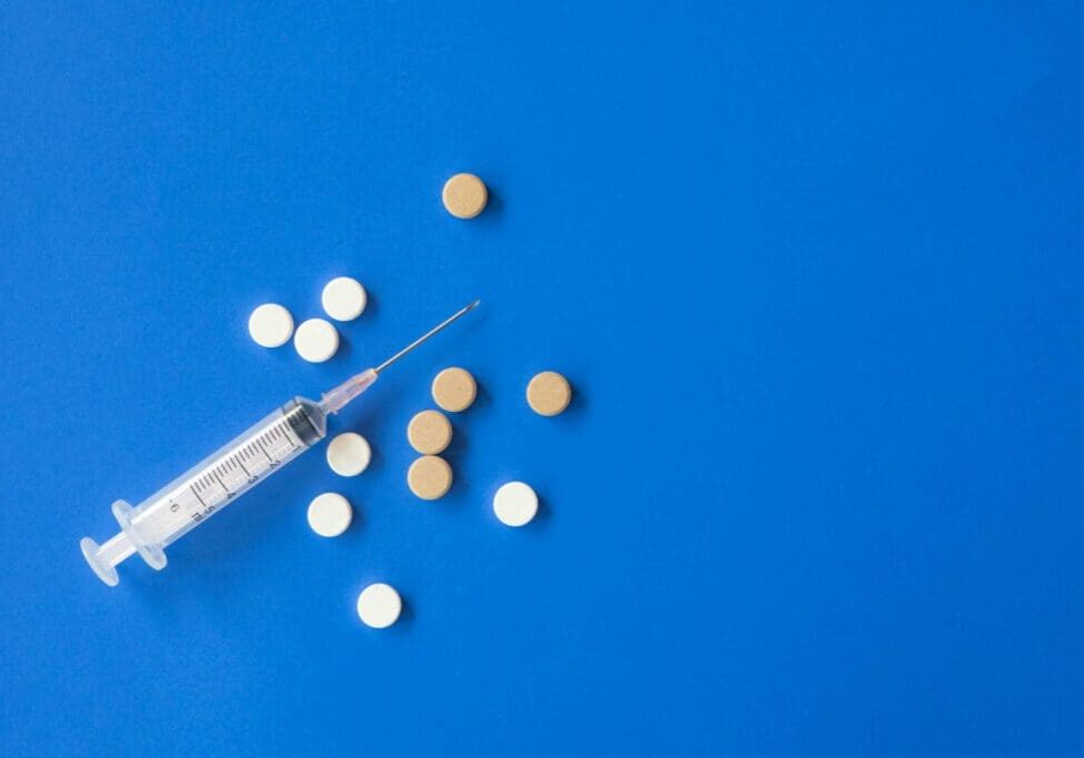 The image displays a syringe and several tablets placed on a blue sheet.
