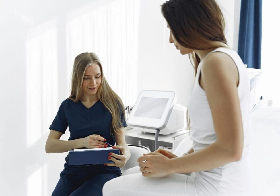 Medical specialist in blue scrubs discussing a treatment plan with a patient in a clinical setting.