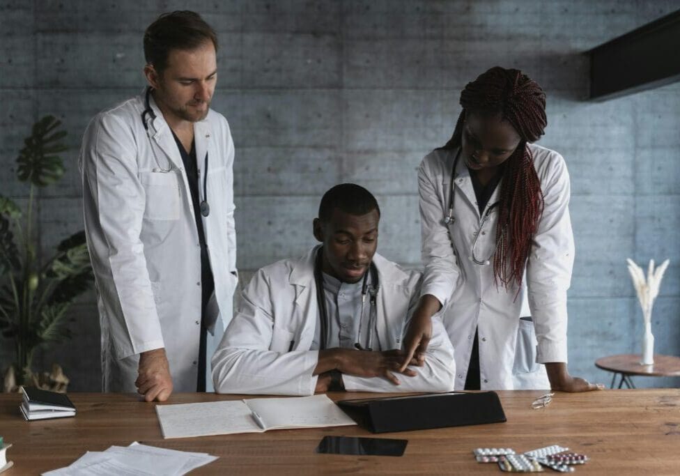 A group of three healthcare providers consulting over patient reports in a clinic.