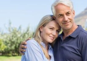 The image shows a middle-aged couple outdoors, embracing each other