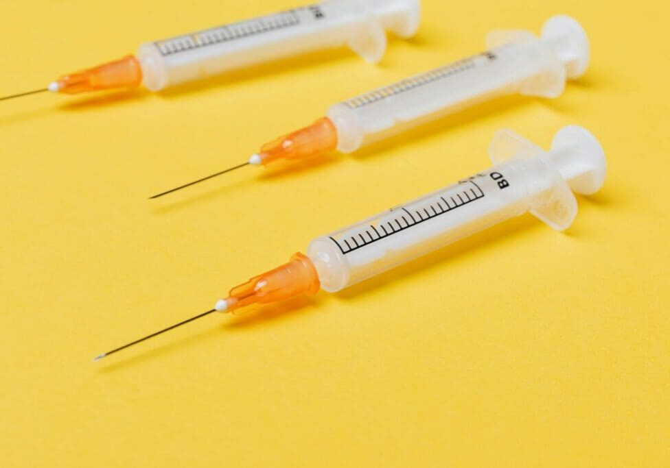 The image shows three medical syringes with needles on a yellow background.